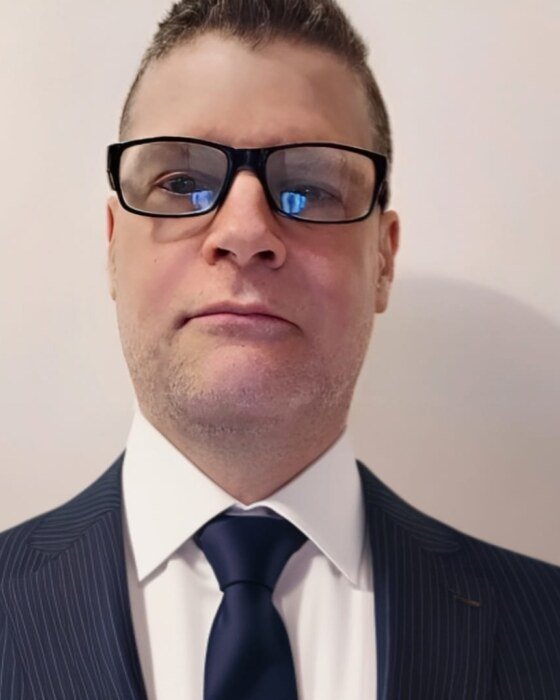 Portrait of author Michael Clark in a dark suit and glasses.